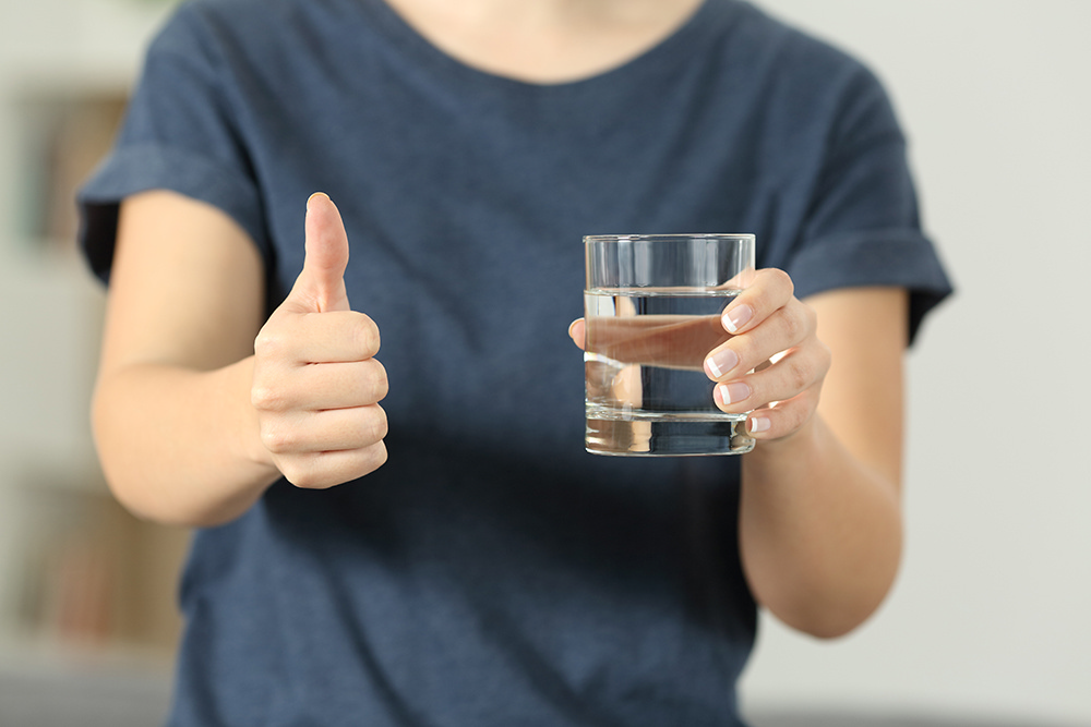Person med vandglas, der giver tommel-up