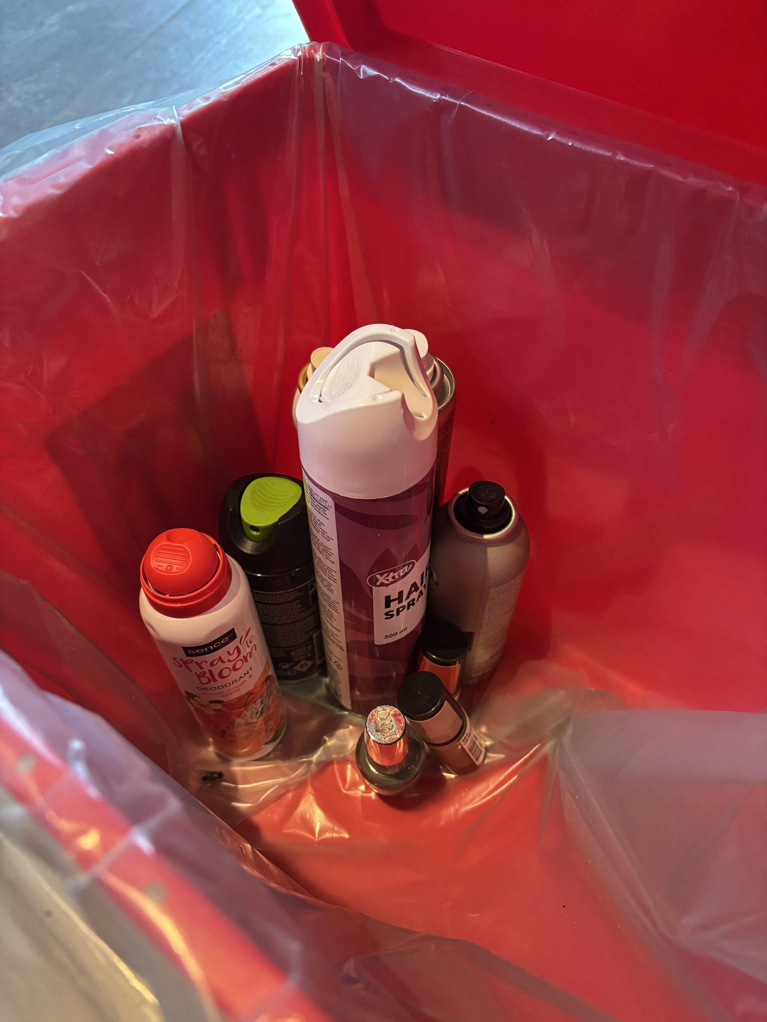 Miljøkasse foret med plastikpose indeholdende hårspray og neglelak.